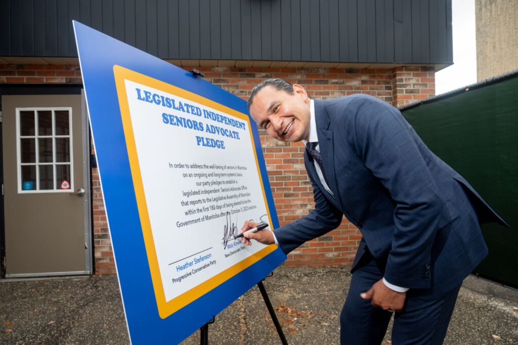 Premier Wab Kinew signing Seniors' Advocate Act at [location], surrounded by MSEAC members
